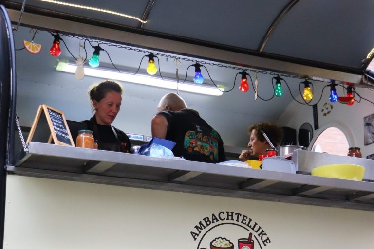 Familie Stam foodtruck Drie mensen werken in een foodtruck met kleurrijke verlichting.